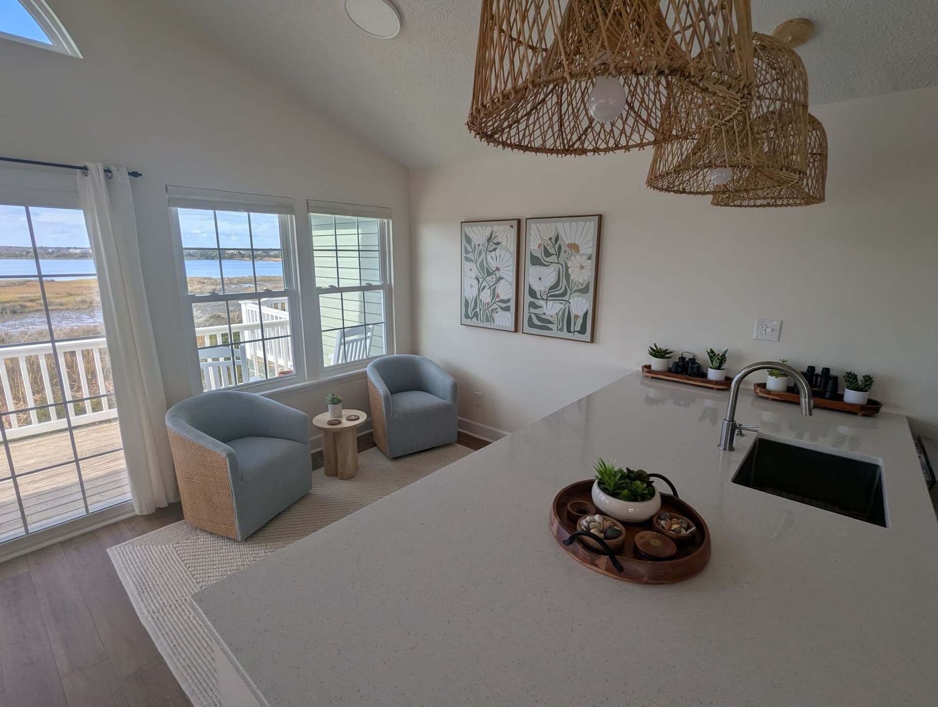 View across a white kitchen island toward two blue chairs by the window overlooking the marsh.